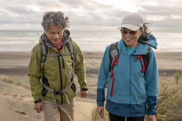 couple with wind breaker coats walking on beach